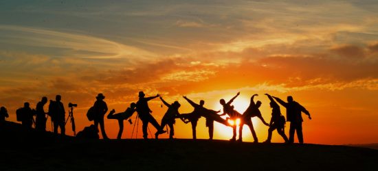 Group of people silhouetted against a vibrant sunset, showcasing unity and joy.