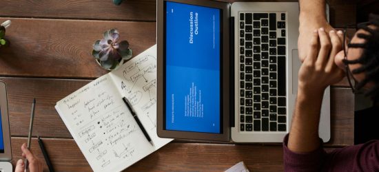 Group of coworkers discussing business strategies with laptops and tablets in a modern office setting.